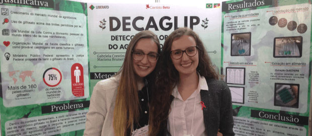As jovens cientistas Gabriela Delela e Mariana Buttenbender em frente ao banner explicativo do projeto DECAGLIP