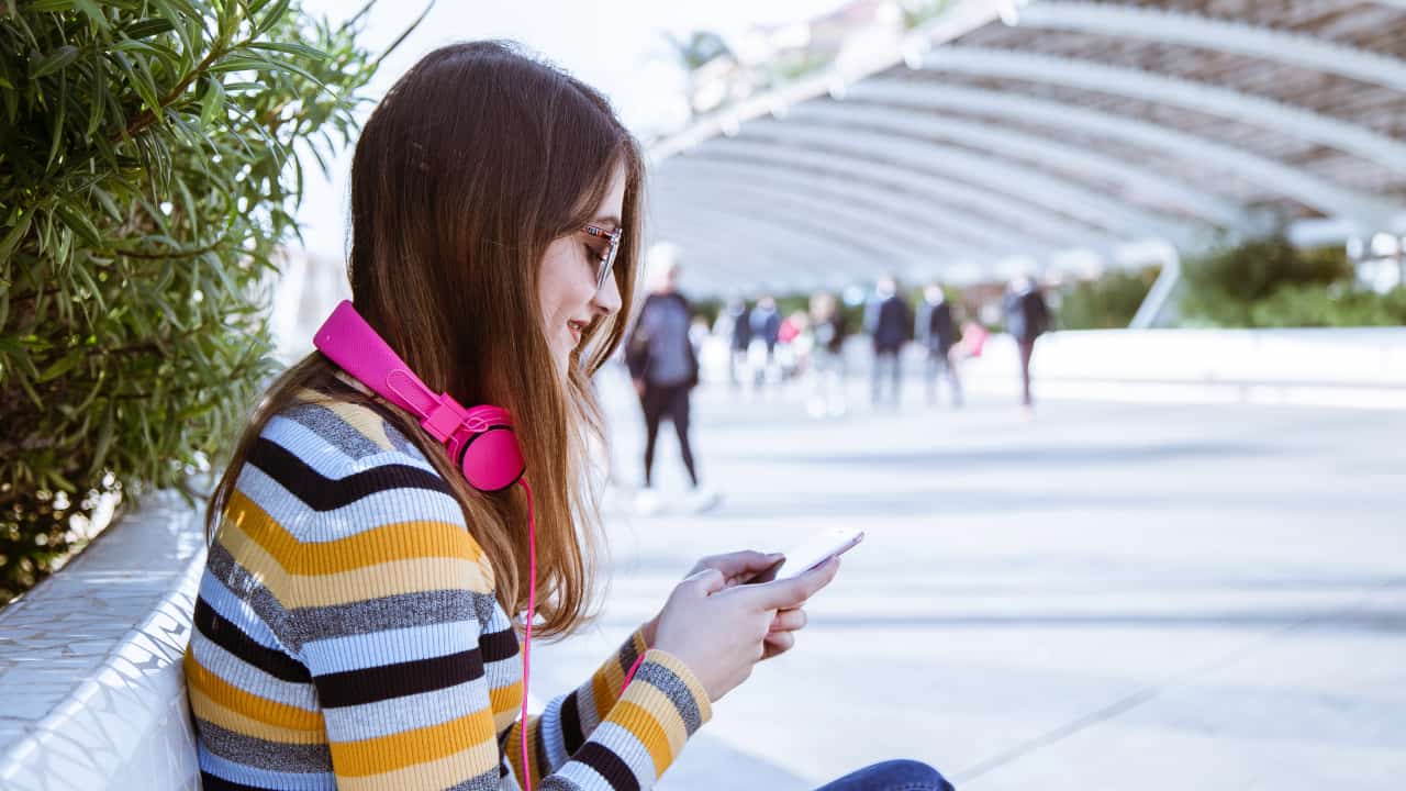 Pessoa sentada com fone de ouvido mexendo no celular