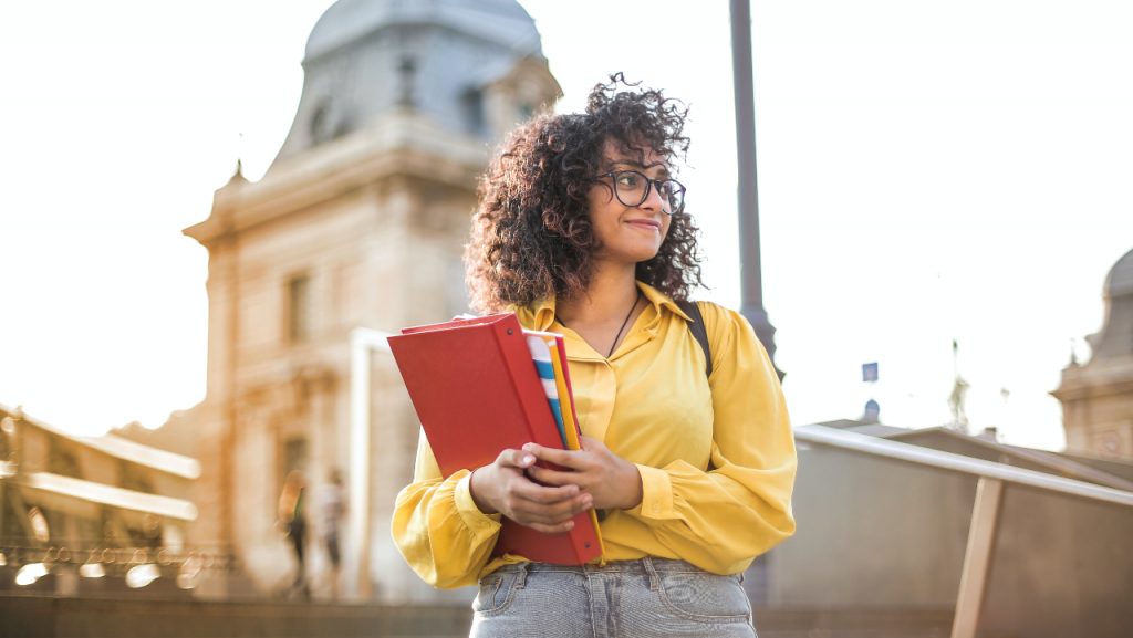 moça de amarelo segurando fichário vermelho - bolsas de intercâmbio na graduação